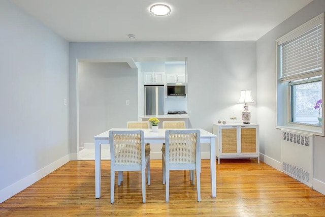 dining room with light wood-type flooring, baseboards, and radiator