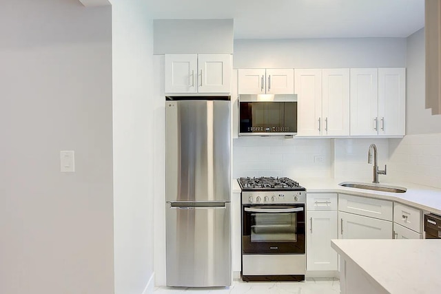 kitchen with white cabinets, a sink, marble finish floor, light countertops, and appliances with stainless steel finishes