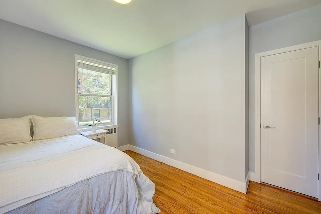 bedroom with light wood-style floors, radiator heating unit, and baseboards