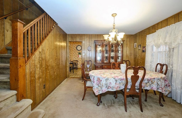 carpeted dining space with stairway, wood walls, and a notable chandelier