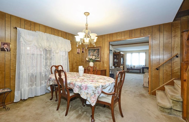 dining space featuring light colored carpet, stairs, a chandelier, and wooden walls