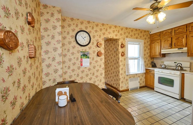 kitchen featuring white gas range, light tile patterned floors, light countertops, radiator, and under cabinet range hood