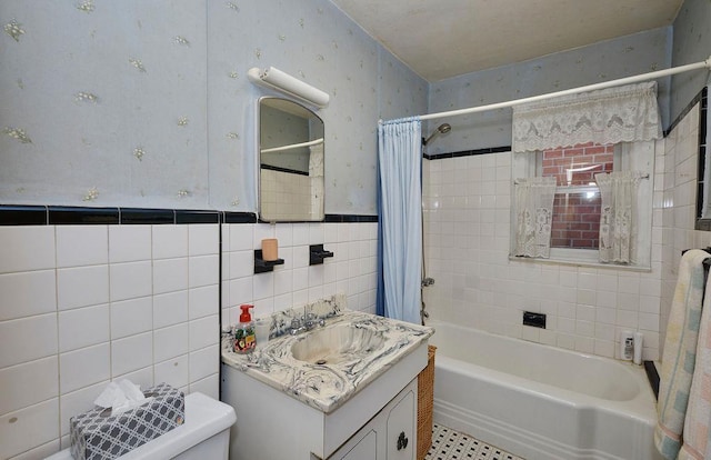 full bathroom featuring toilet, wainscoting, tile walls, wallpapered walls, and shower / tub combo with curtain