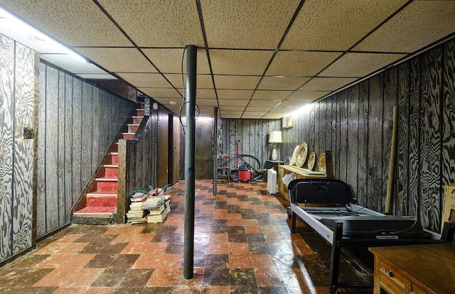 finished below grade area with wood walls, stairway, and a drop ceiling