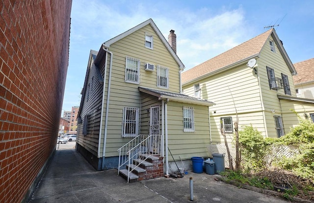 back of house with a chimney and a wall mounted AC