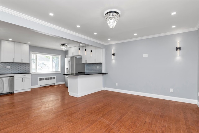 kitchen with appliances with stainless steel finishes, radiator heating unit, dark countertops, and tasteful backsplash