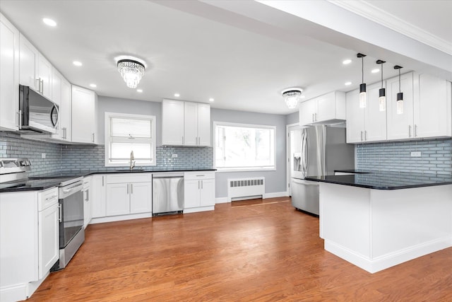 kitchen with tasteful backsplash, stainless steel appliances, radiator, dark countertops, and a peninsula