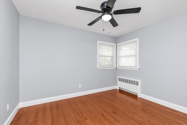 empty room featuring radiator, a ceiling fan, wood finished floors, and baseboards