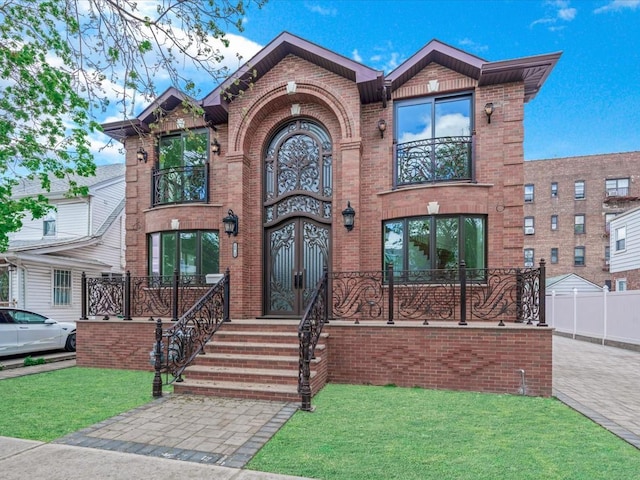 view of front of house featuring a balcony, a front yard, and brick siding