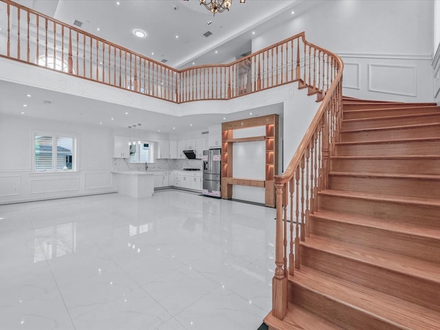 stairway featuring recessed lighting, a high ceiling, a decorative wall, and an inviting chandelier