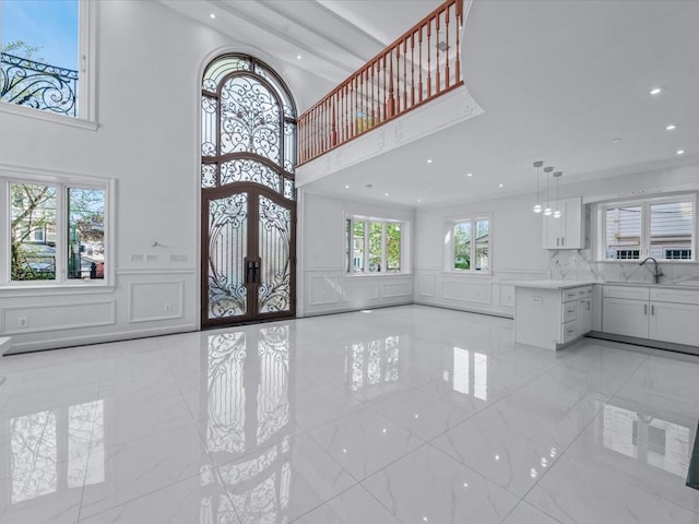 unfurnished living room with french doors, a sink, a high ceiling, a decorative wall, and recessed lighting
