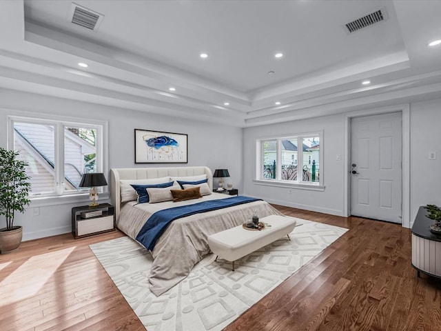 bedroom with baseboards, a tray ceiling, visible vents, and wood finished floors