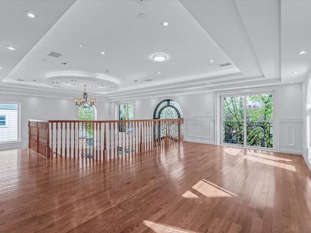 unfurnished living room featuring a raised ceiling, a decorative wall, and a chandelier