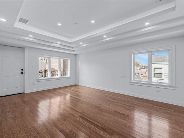 unfurnished living room with visible vents, wood finished floors, baseboards, recessed lighting, and a tray ceiling