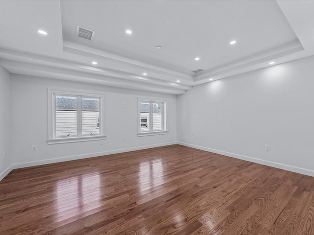 empty room featuring recessed lighting, a tray ceiling, visible vents, and wood finished floors