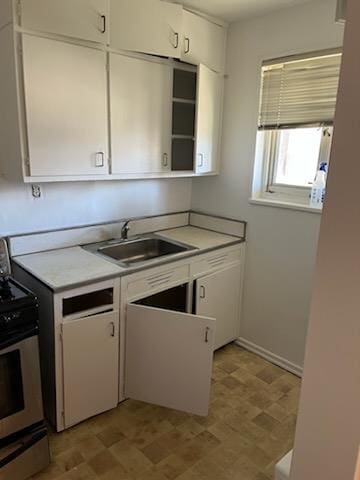 kitchen with a sink, stainless steel gas stove, light countertops, and white cabinets