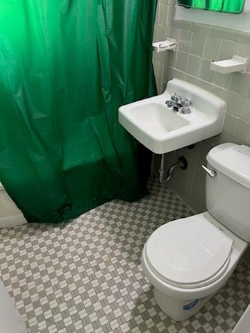 bathroom featuring toilet, a shower with curtain, tile walls, and tile patterned floors