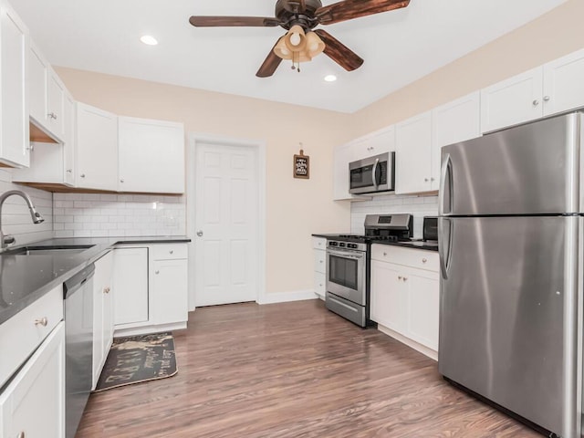 kitchen with white cabinetry, a sink, appliances with stainless steel finishes, ceiling fan, and dark countertops