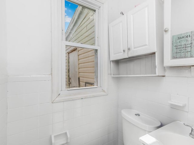 half bathroom with toilet, tile walls, and a sink