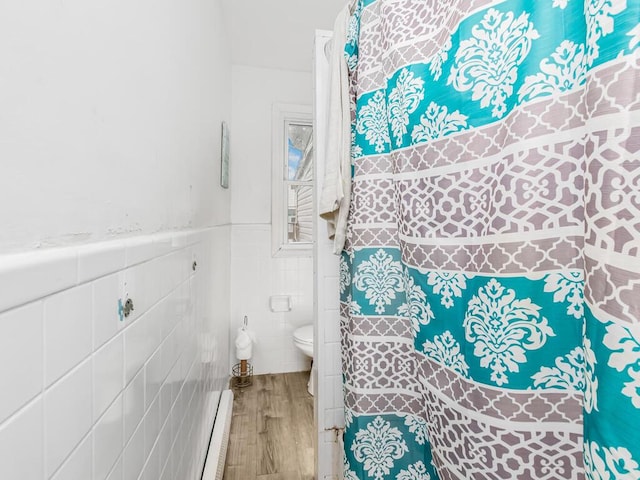 bathroom with a baseboard heating unit, toilet, tile walls, wood finished floors, and wainscoting