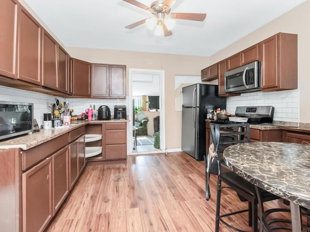 kitchen with light wood-style flooring, appliances with stainless steel finishes, ceiling fan, light stone countertops, and backsplash