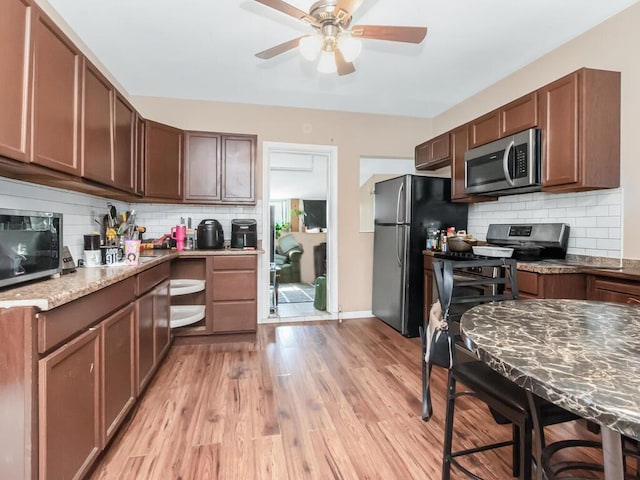 kitchen with appliances with stainless steel finishes, light wood-style floors, ceiling fan, light stone countertops, and backsplash