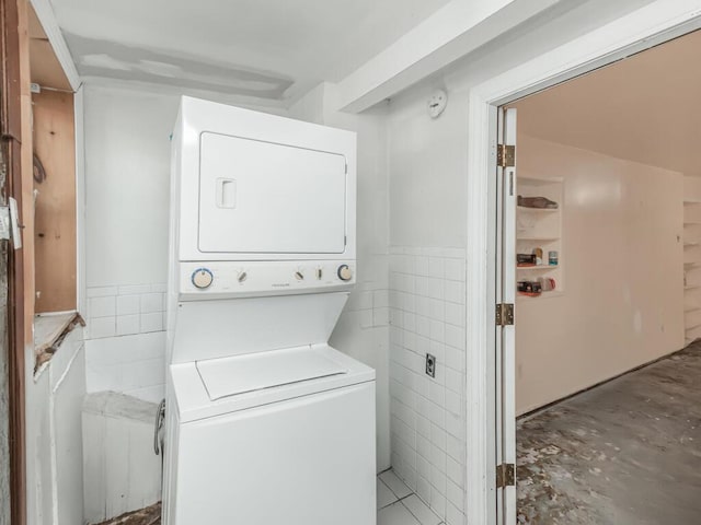 laundry area featuring stacked washer / dryer, a wainscoted wall, tile walls, and laundry area