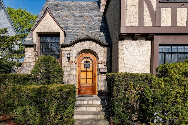 view of exterior entry with stucco siding, a high end roof, and stone siding