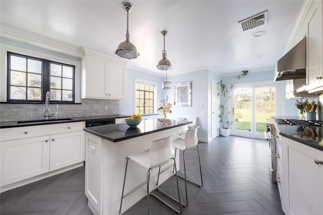 kitchen featuring exhaust hood, high end stove, a sink, a kitchen breakfast bar, and visible vents