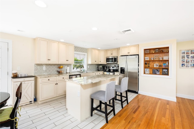 kitchen with stainless steel appliances, cream cabinetry, decorative backsplash, and a sink