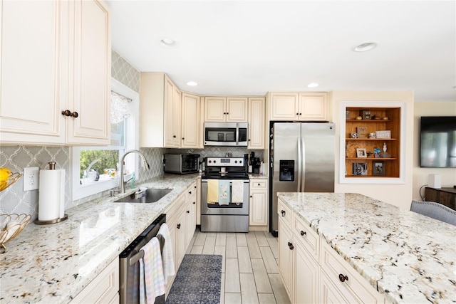 kitchen with cream cabinets, tasteful backsplash, light stone counters, a sink, and appliances with stainless steel finishes