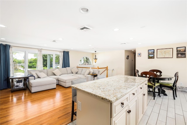 kitchen featuring light stone counters, light wood finished floors, a kitchen breakfast bar, a kitchen island, and visible vents