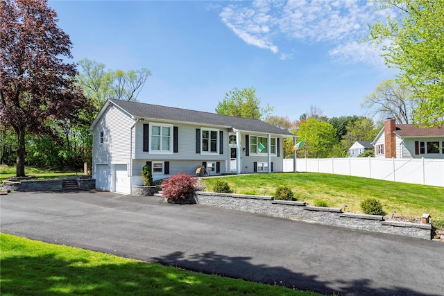 bi-level home featuring a front yard, aphalt driveway, an attached garage, and fence