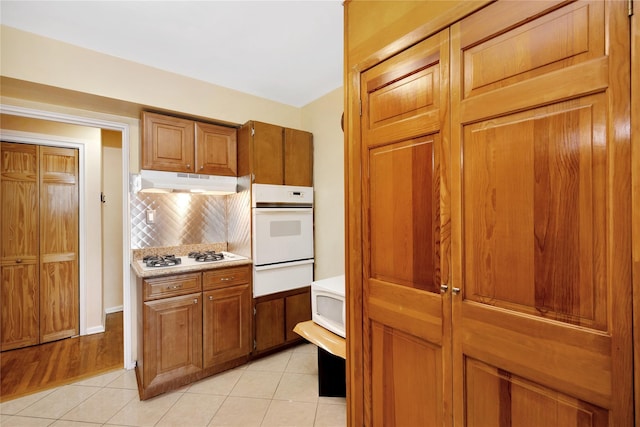 kitchen with under cabinet range hood, white appliances, brown cabinets, and a warming drawer