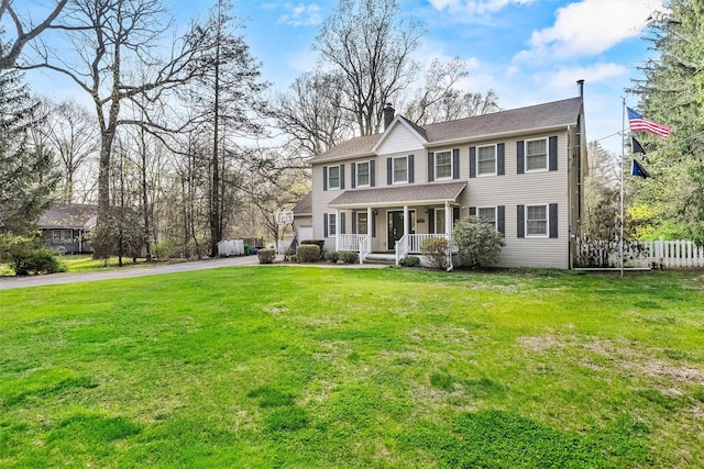 colonial home with aphalt driveway, a chimney, fence, a porch, and a front lawn