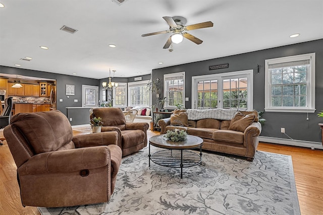 living area with visible vents, light wood-style floors, a baseboard heating unit, recessed lighting, and ceiling fan with notable chandelier