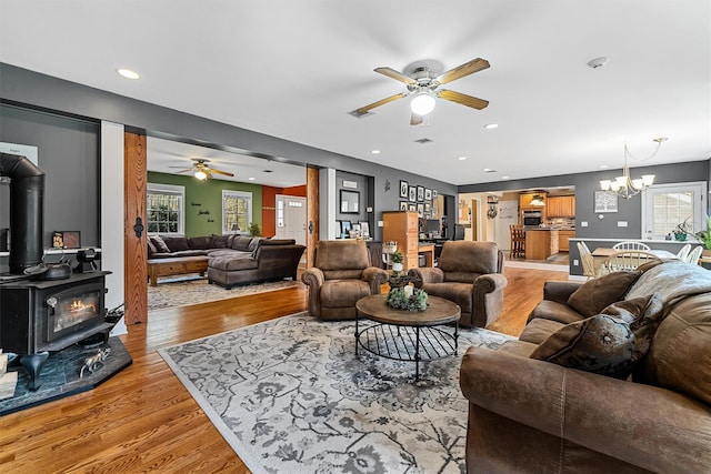 living area featuring a wood stove, visible vents, recessed lighting, light wood finished floors, and ceiling fan with notable chandelier
