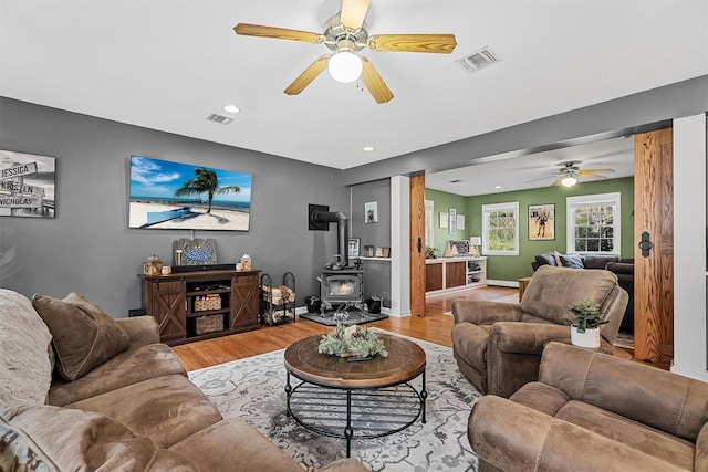living room with a wood stove, ceiling fan, light wood-style floors, and visible vents