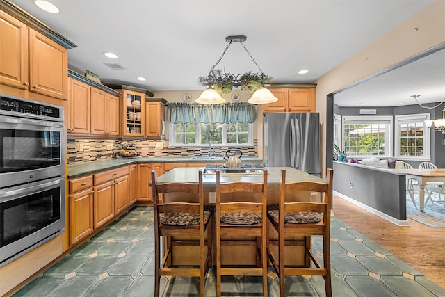 kitchen with tasteful backsplash, glass insert cabinets, a breakfast bar, stainless steel appliances, and visible vents