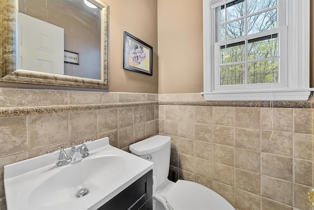 half bathroom with tile walls, a wainscoted wall, toilet, and vanity