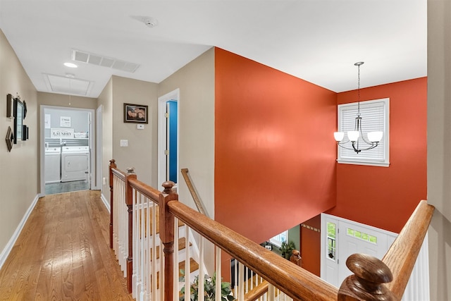 hall with attic access, washing machine and dryer, an upstairs landing, visible vents, and wood finished floors