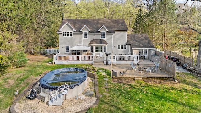 rear view of property with fence, a deck, a yard, and a fenced in pool