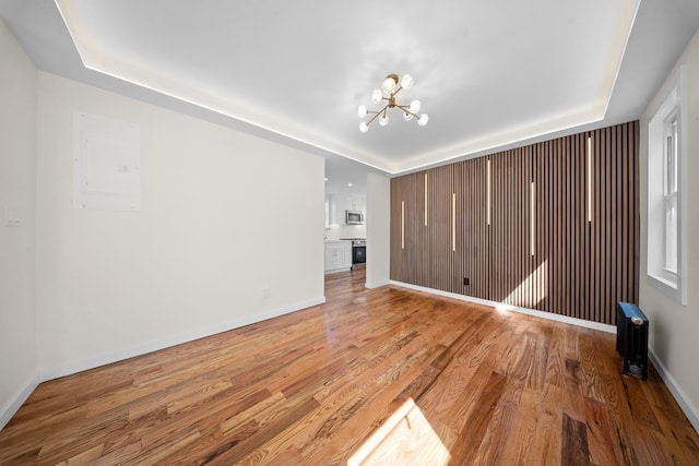 13107 229th St, Laurelton, NY 11413 - unfurnished living room with light wood finished floors, a tray ceiling, a chandelier, and electric panel