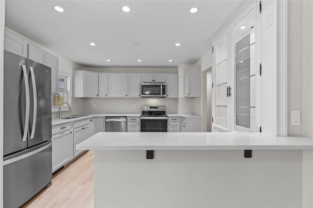 kitchen featuring decorative backsplash, a sink, stainless steel appliances, light countertops, and a peninsula
