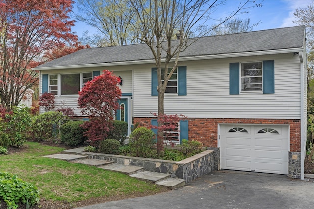 bi-level home featuring brick siding, a shingled roof, an attached garage, and aphalt driveway