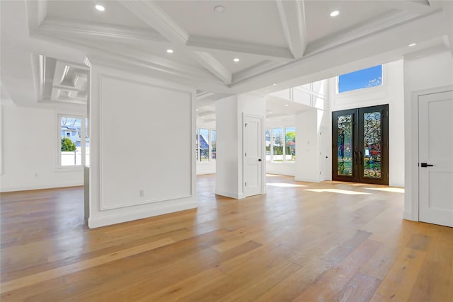 unfurnished living room featuring a wealth of natural light, beam ceiling, french doors, and coffered ceiling