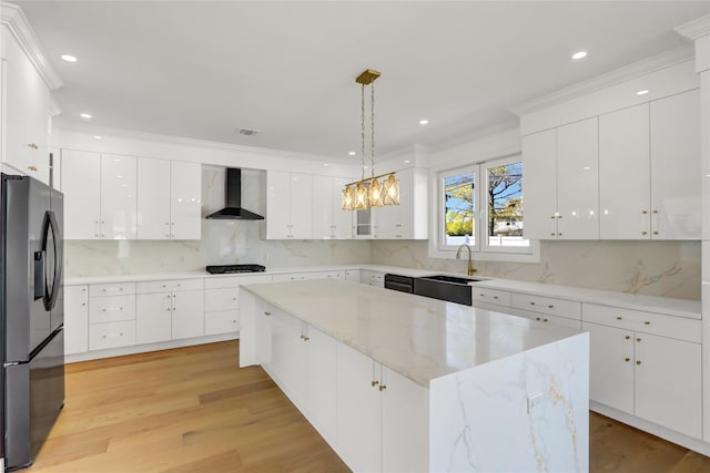 kitchen featuring a center island, a sink, black appliances, light wood-type flooring, and wall chimney exhaust hood