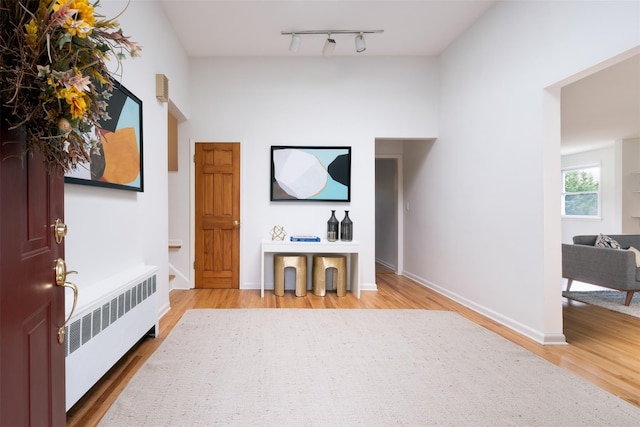 interior space with baseboards, radiator heating unit, rail lighting, and light wood-style flooring