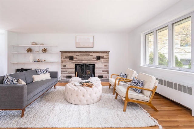 living area with wood finished floors, a stone fireplace, and radiator
