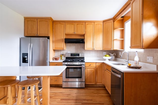 kitchen with a sink, under cabinet range hood, light wood-type flooring, light countertops, and appliances with stainless steel finishes
